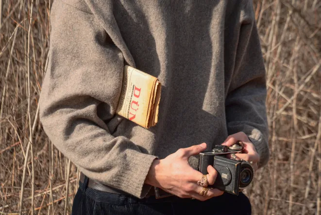 Man in a wool sweater holding a camera and a book