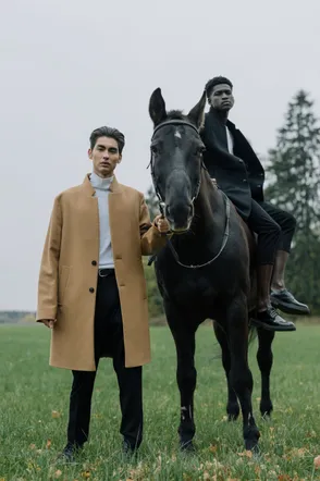 Man in a camel wool coat beside a rider on a black horse